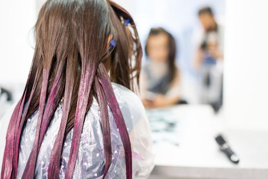 little girl dyes her hair purple in a hairdressing salon