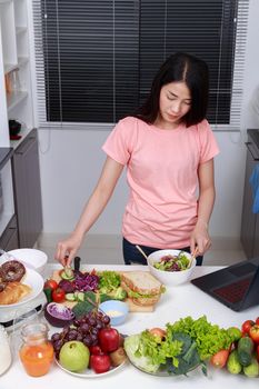 young woman mixing salad while cooking with laptop in kitchen 