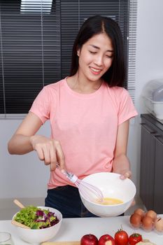 woman cooking and whisking eggs in a bowl in kitchen room