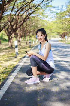 young sporty woman sitting on the road in the park and using smartphone with earphone to listening music