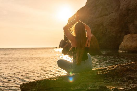 Young woman in swimsuit with long hair practicing stretching outdoors on yoga mat by the sea on a sunny day. Women's yoga fitness pilates routine. Healthy lifestyle, harmony and meditation concept.