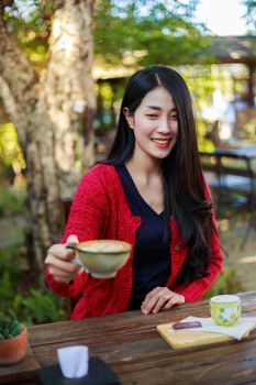 young woman sitting on a table and drinking a cup of coffe in the garden