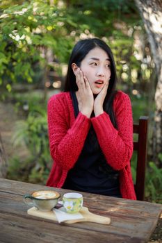 Portrait of a shocked young woman sitting on table with coffee in the garden