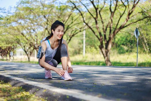 young sporty woman tying shoelaces while listening to music with earphones from her smartphone in the park 