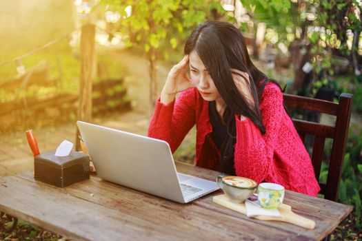 worried woman using laptop and drinking coffee in the garden