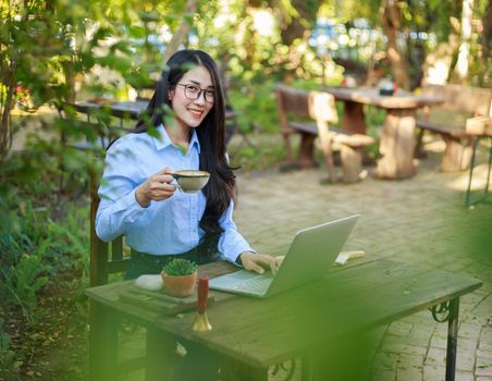 young woman drinking coffee and working with laptop in the garden