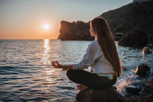 Young woman in swimsuit with long hair practicing stretching outdoors on yoga mat by the sea on a sunny day. Women's yoga fitness pilates routine. Healthy lifestyle, harmony and meditation concept.