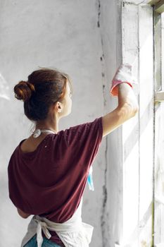 Woman in a white apron paints a window in a house interior renovation. High quality photo