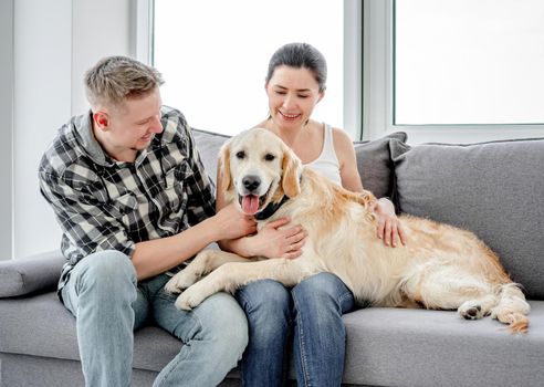 Beautiful woman and man cuddling cute dog in light room