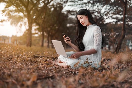 beautiful woman using laptop and mobile phone in the outdoor park