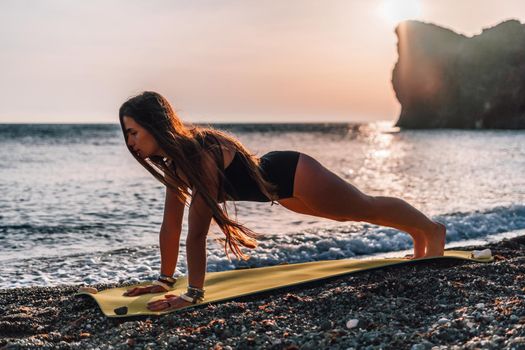 Young woman in swimsuit with long hair practicing stretching outdoors on yoga mat by the sea on a sunny day. Women's yoga fitness pilates routine. Healthy lifestyle, harmony and meditation concept.