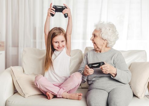 Smiling grandmother with little granddaughter playing games together with gamepads