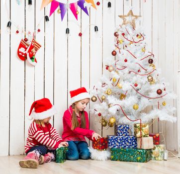 two little girls open christmas presents sitting on the floor near decorated new year tree