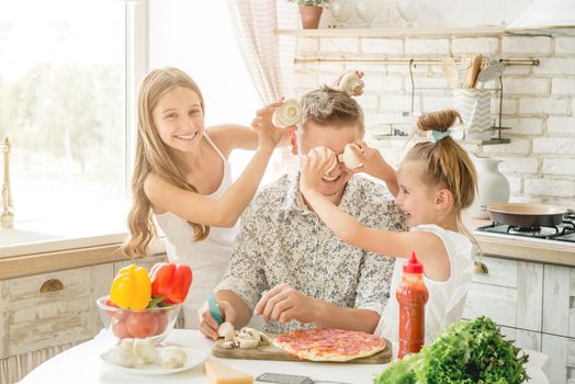 Dad with two small daughters preparing pizza with mushrooms in the kitchen