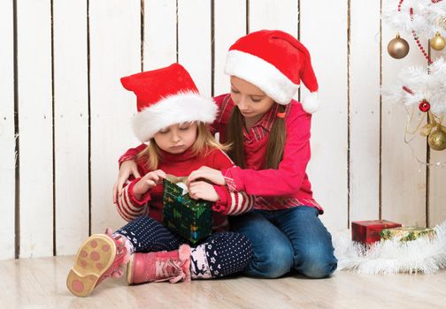 two little girls in red hats sitting on the floor with gifts near new year tree