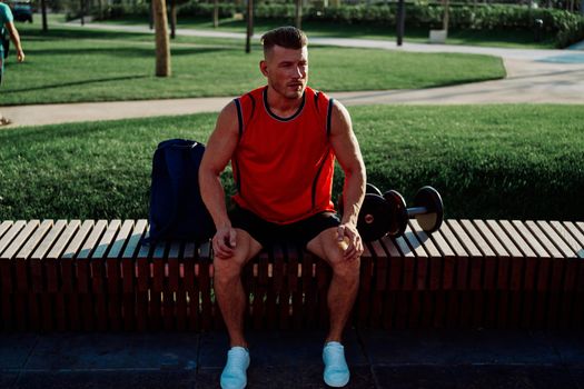 Cheerful male athlete in the park sits on a bench. High quality photo