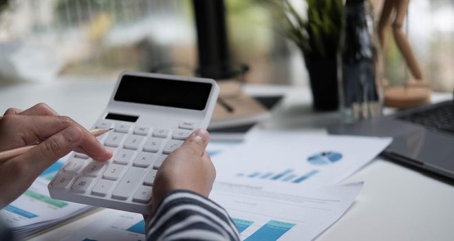 Close up woman planning budget, using calculator and laptop, reading documents, young female checking finances, counting bills or taxes, online banking services, sitting at desk.