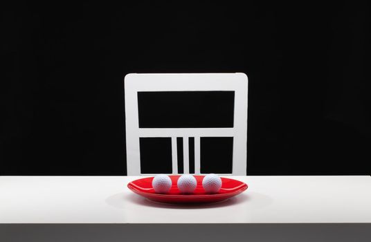 Three white golf balls on the red plate. White old chair and white table in the dark room.