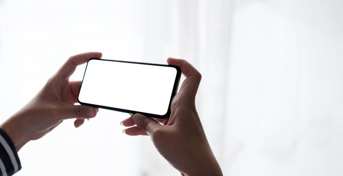 Mockup image blank white screen cell phone.women hand holding texting using mobile on desk at home office..