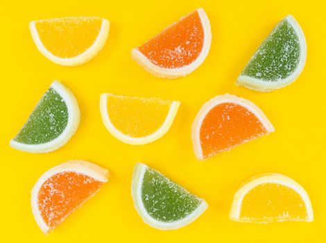 Multicolored marmalade citrus slices in sugar on a yellow background.