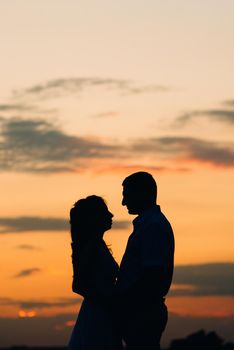 silhouettes of a happy young couple guy and girl on a background of orange sunset in the ocean