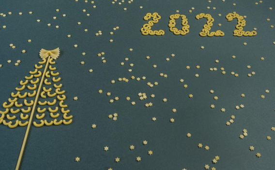 Christmas tree lined with dry pasta and numbers 2022 and stars from pasta on a green paper background