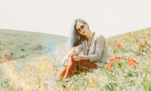 Beautiful young woman in sunglasses sitting on red tulip meadow on sunny day, looking at camera.