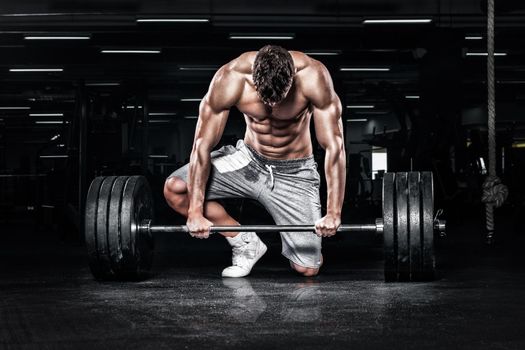 Athletic shirtless young sports man - fitness model with barbell in gym.