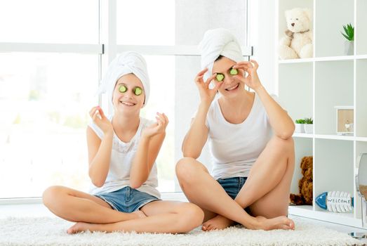 Funny cheerful young mother and her cute teen daughter with cucumber masks on