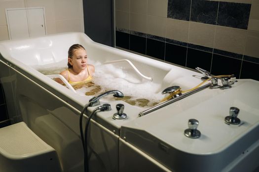 a little girl takes the procedure in a mineral bath. The patient receives water treatments with a mineral pearl bath.