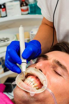 Dental practice, the dentist removes stones and hard plaque from the teeth with the help of ultrasound,patient with retractor and saliva ejector in the mouth.2020