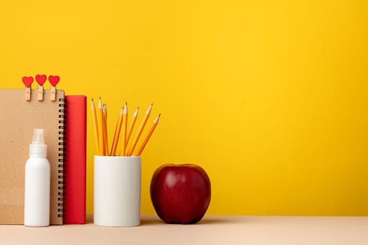 Cup of pencils and notepads on desk against yellow background, front view