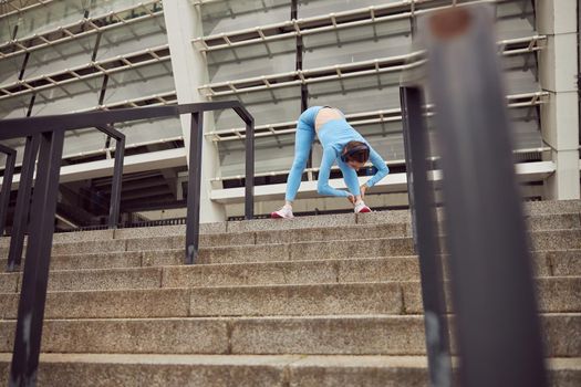 Beautiful fit caucasian woman is doing exercises outdoors at the city