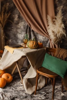 Autumn interior: a table covered with dishes, pumpkins, chair, casual arrangement of Japanese pampas grass. Interior in the photo Studio.