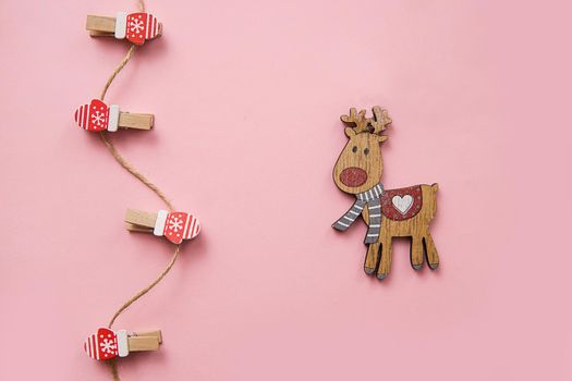 Christmas decorations decorative background. Decorative pins in the form of red gloves and a wooden deer on a pink background. Top view, minimalism, flat layout.