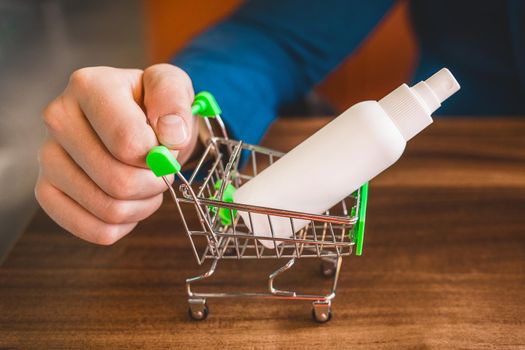 Businessman hand rolls small shopping cart with antiseptic, close-up.