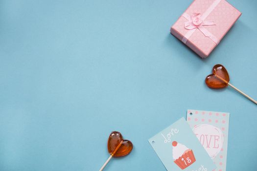 Lollipops in the form of hearts, a gift and greeting card on a blue background. Valentine's day, top view. Copy space. Mortgage the apartment. Text phrase Love and Love is sweet.