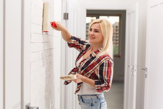 Woman painting wall in new home. Happy beautiful young woman doing wall painting. A young girl makes repairs: paints the walls with white paint using a roller.