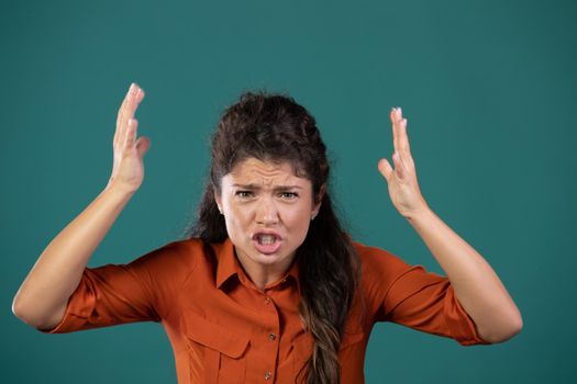 Portrait of angry woman yelling, holding hands up in air, against blue background in studio