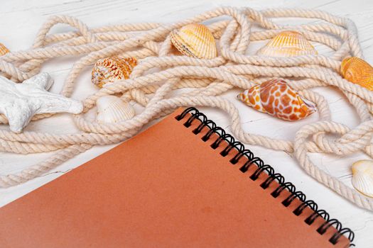 Close up photo of brown notepad with sea shells on wooden planks closeup, copy space