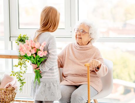 Little girl with bouquet of tulips for great-grandmother indoors