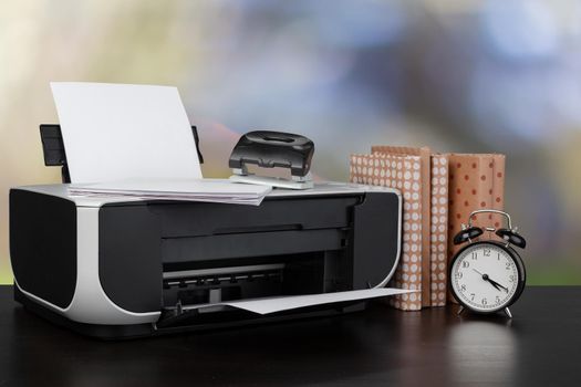 Compact home printer on desk with books against blurred background, close up