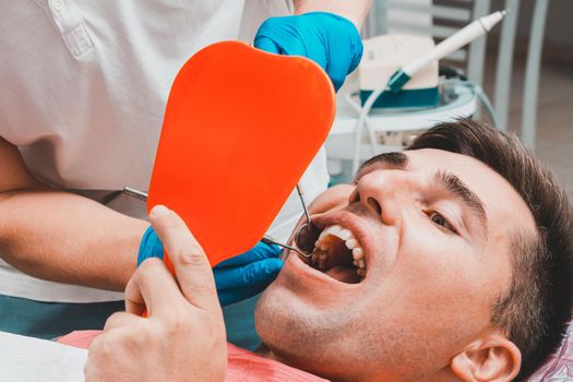 The patient at the dentist,a man holds a mirror in his hands, assesses the condition of his teeth.2020