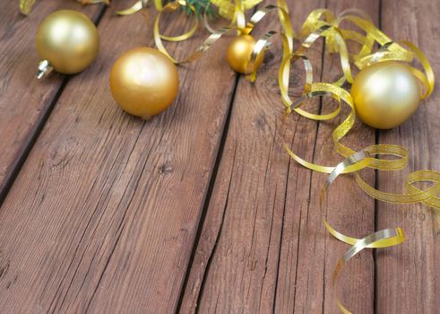 Christmas composition of yellow Christmas balls, fir branches, and a gold ribbon on a brown wooden background