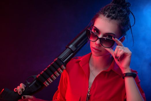 bright brunette in a red jumpsuit with a shotgun on a dark background in neon light