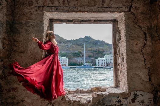 View of Balaklava Bay through an arched balcony in oriental style. The girl in a long red dress stands with her back. Abandoned mansion on the Black Sea coast.