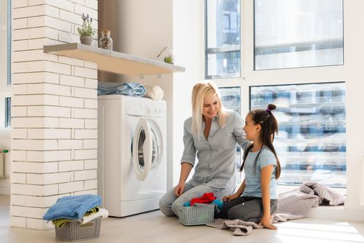 Happy housewife and her daughter with linen near washing machine