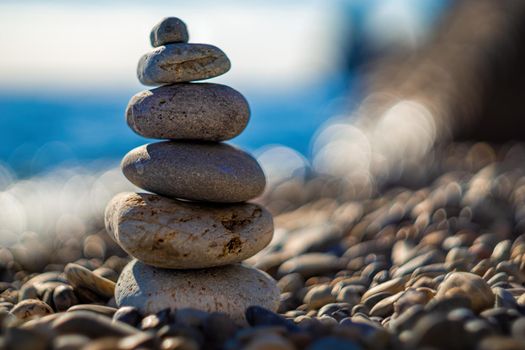 Balanced Pebbles Pyramid on the Beach on Sunny Day and Clear Sky at Sunset. Blue Sea on Background Selective focus, zen stones on sea beach, meditation, spa, harmony, calm, balance concept.