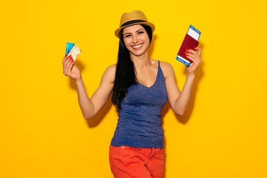 Young smiling excited woman student holding passport boarding pass ticket and credit card isolated on yellow background. Air travel flight - Image