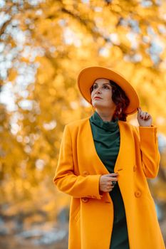 Beautiful woman walks outdoors in autumn. She is wearing a yellow coat, yellow hat and green dress. Young woman enjoying the autumn weather. Autumn content.